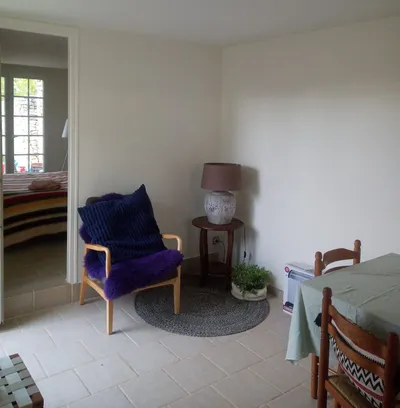 Coin salon repeint en blanc cassé, fauteuil avec plaid violet et vue vers la chambre