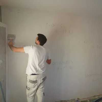 Artisan de dos enduisant un mur à la taloche, inscriptions de l'ancien mur visibles en transparence
