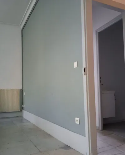 Chambre avec pan de mur gris-bleu repeint, plinthes blanches et vue vers la salle de bains