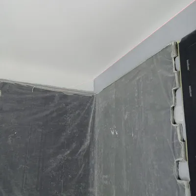 Angle de pièce protégé par des bâches grises, plafond déjà repeint en blanc