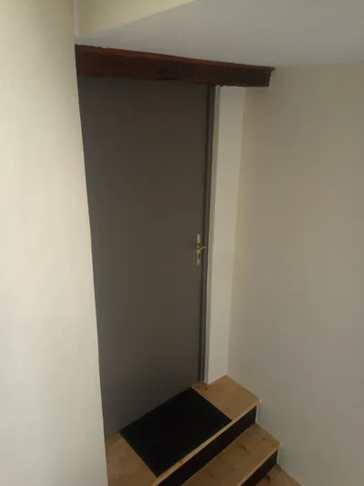 Petite porte grise sous l'escalier, linteau en bois et murs repeints en crème