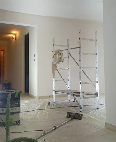Pièce en préparation avec bâches, aspirateur de chantier et échafaudage, murs blancs finis