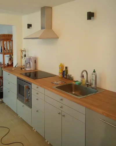 Cuisine ouverte avec murs blancs repeints, plan de travail en bois et façades gris-bleu
