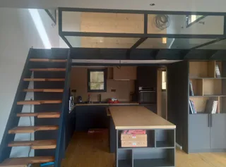 Mezzanine avec escalier et structure en acier laqué noir surplombant une cuisine ouverte