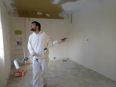 Peintre appliquant une peinture blanche au plafond avec un rouleau à rallonge, travail en cours