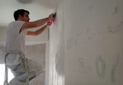 Artisan lissant un enduit sur un mur depuis un escabeau, finition en cours