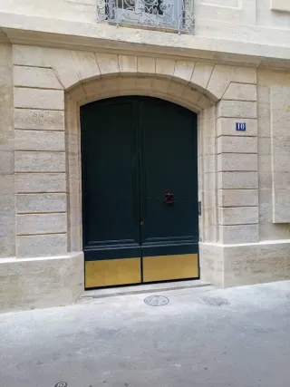 Dark green lacquered double door with gold base panels on a stone facade