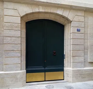 Porte cochère laquée vert foncé avec soubassement doré sur une façade en pierre