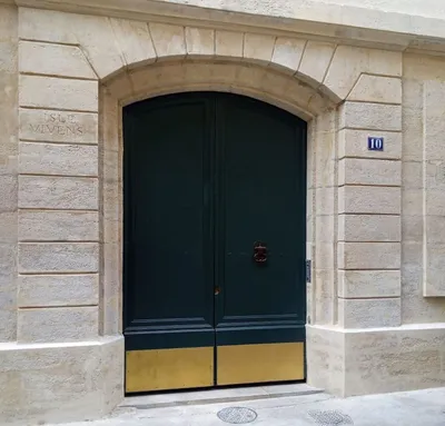Porte cochère laquée vert foncé avec soubassement doré sur une façade en pierre