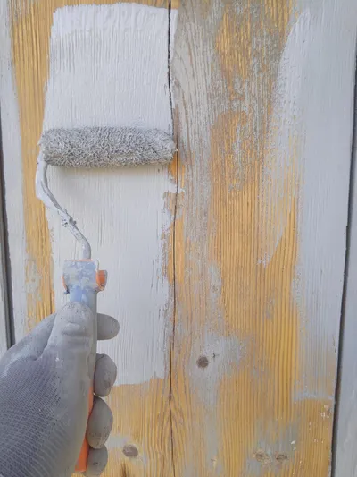 Gros plan d'un rouleau appliquant du blanc sur un vieux bois peint en jaune