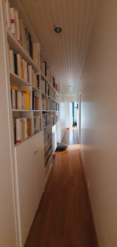 Couloir étroit aux murs et plafond blancs fraîchement peints, bibliothèque intégrée, parquet au sol