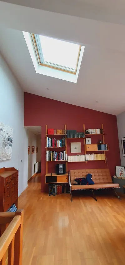 Salon avec mur d'accent rouge terracotta peint, velux au plafond et vue sur le couloir