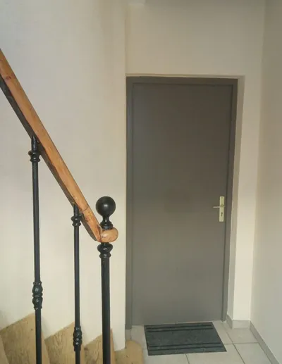 Palier d'escalier avec porte grise repeinte et murs beiges, rampe en bois