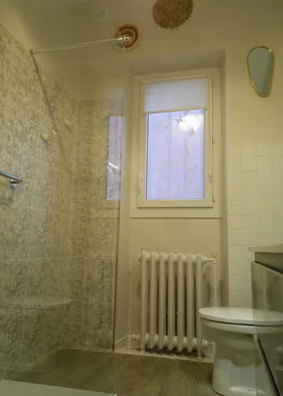 Salle de bain avec papier peint à motifs dans la douche et carrelage blanc