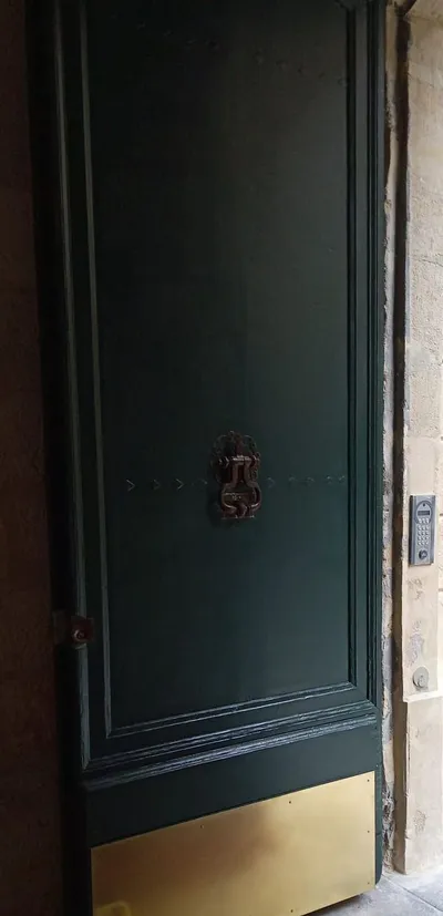 Porte extérieure vert foncé en cours de peinture sur façade en pierre, heurtoir et soubassement doré
