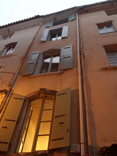 Façade en pierre avec volets peints gris-vert, vue en contre-plongée, lumière du soir
