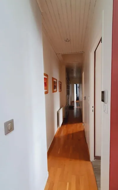 Couloir aux murs blancs fraîchement peints, parquet bois et mur rouge au fond
