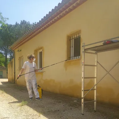 Artisan traitant à la lance une façade jaune, échafaudage et toit de tuiles