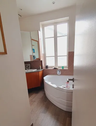 Salle de bains avec baignoire d'angle, carrelage rose et sol imitation bois
