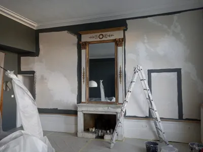 Salon en travaux, murs anthracite et blanc en cours de peinture autour d'une cheminée en marbre