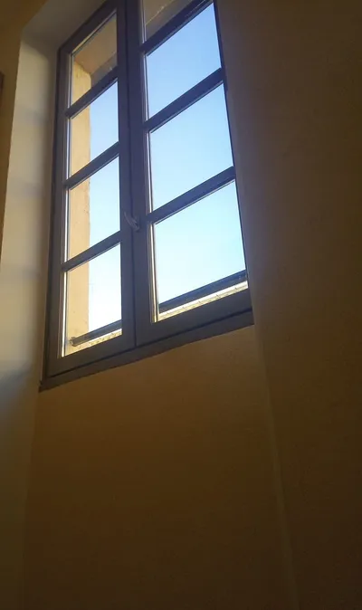 Cage d'escalier aux murs ocres avec une fenêtre ouverte sur le ciel bleu