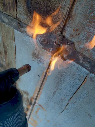 Décapage au chalumeau d'un volet en bois, flamme au ras de l'ancienne peinture