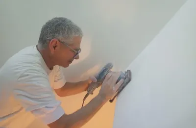 Gros plan d'un artisan qui ponce un angle de mur avant la mise en peinture