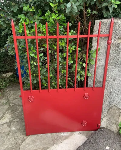 Portail en fer forgé repeint en rouge vif, installé dans un jardin