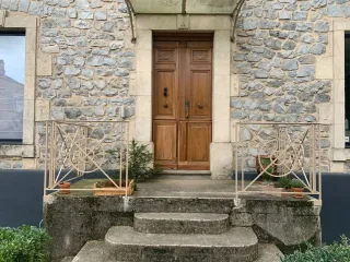 Wide view of a stone entrance with a wooden door and repainted cream railings