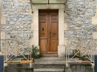 Vue d'ensemble d'une entrée en pierre avec porte en bois et rambardes crème repeintes