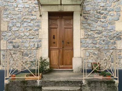 Vue d'ensemble d'une entrée en pierre avec porte en bois et rambardes crème repeintes