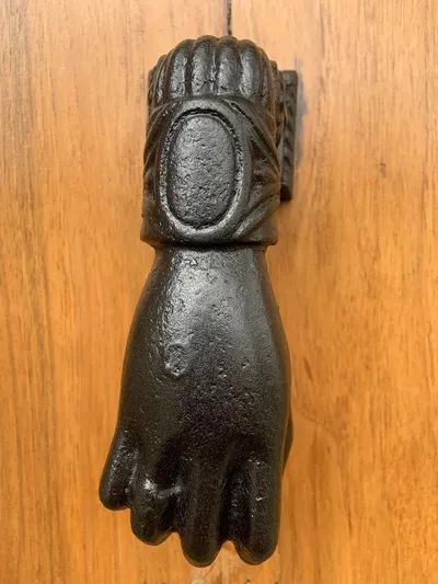 Gros plan d'un heurtoir en forme de main, laqué noir, sur une porte en bois