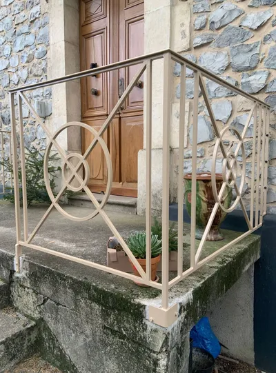 Rambarde en fer forgé crème avec motif circulaire, devant une porte en bois massif