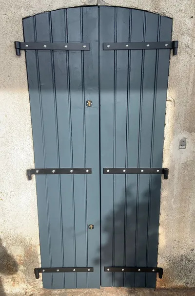 Volets doubles en bois repeints en gris bleuté, avec ferrures noires apparentes