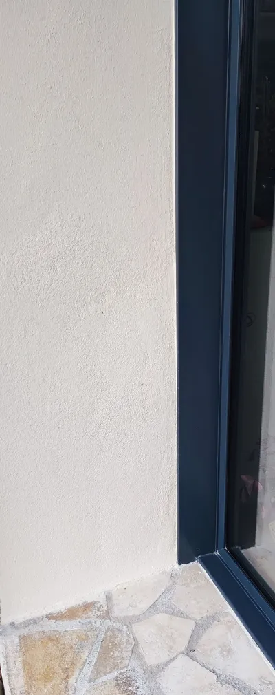 Gros plan d'un enduit de façade beige clair, angle près d'une baie anthracite