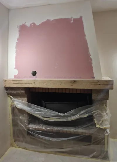 Enduit de rebouchage rose en cours au-dessus d'une cheminée protégée par une bâche