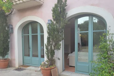 Façade en enduit rose avec deux portes-fenêtres cintrées peintes en vert sauge