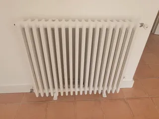 Radiateur à colonnes repeint en blanc dans une pièce au carrelage terre cuite